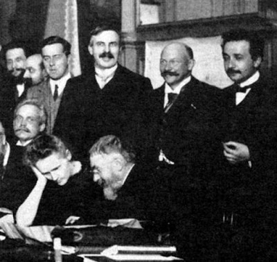 Henri Poincaré discute algo con Marie Sklodowska Curie mientras detrás, de pie, está Albert Einstein en la foto oficial de la Conferencia Solvay de 1911.